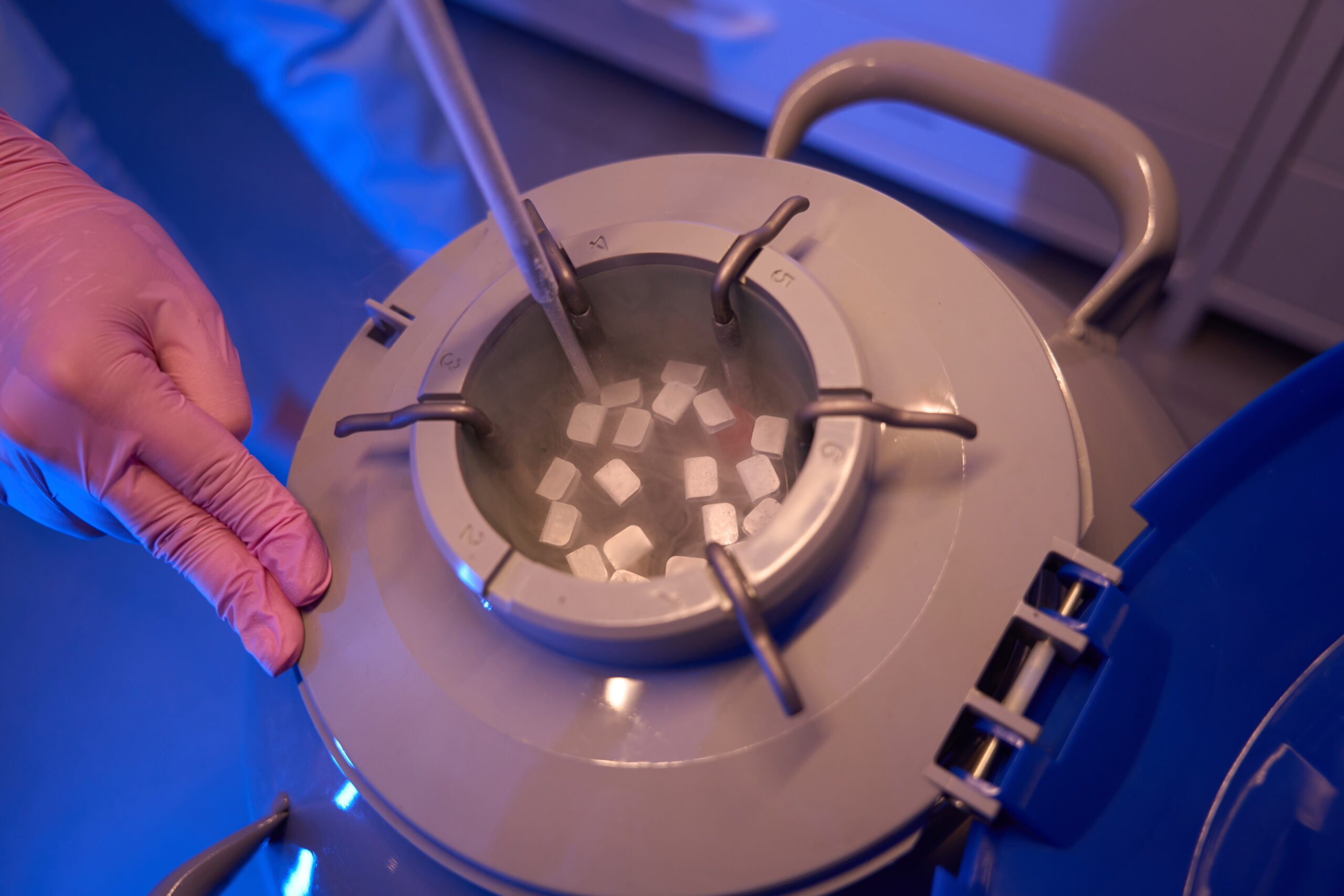 Closeup of gloved hand dipping sealed biological specimens into liquid nitrogen container